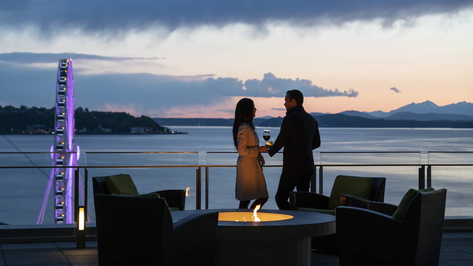 A couple holds hands and shares wine on the balcony as the sun sets