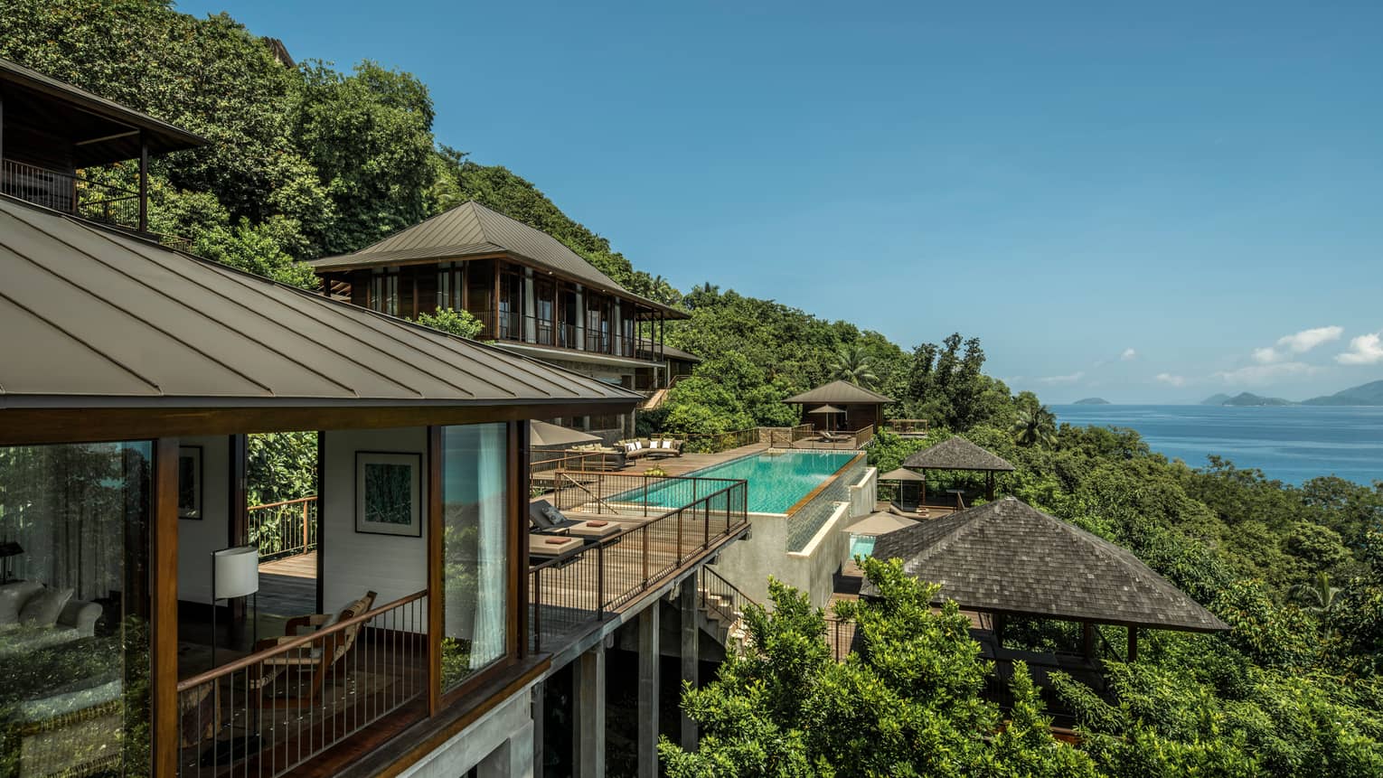 Four-Bedroom Residence Villa roofs, patios amid trees on mountain, ocean below