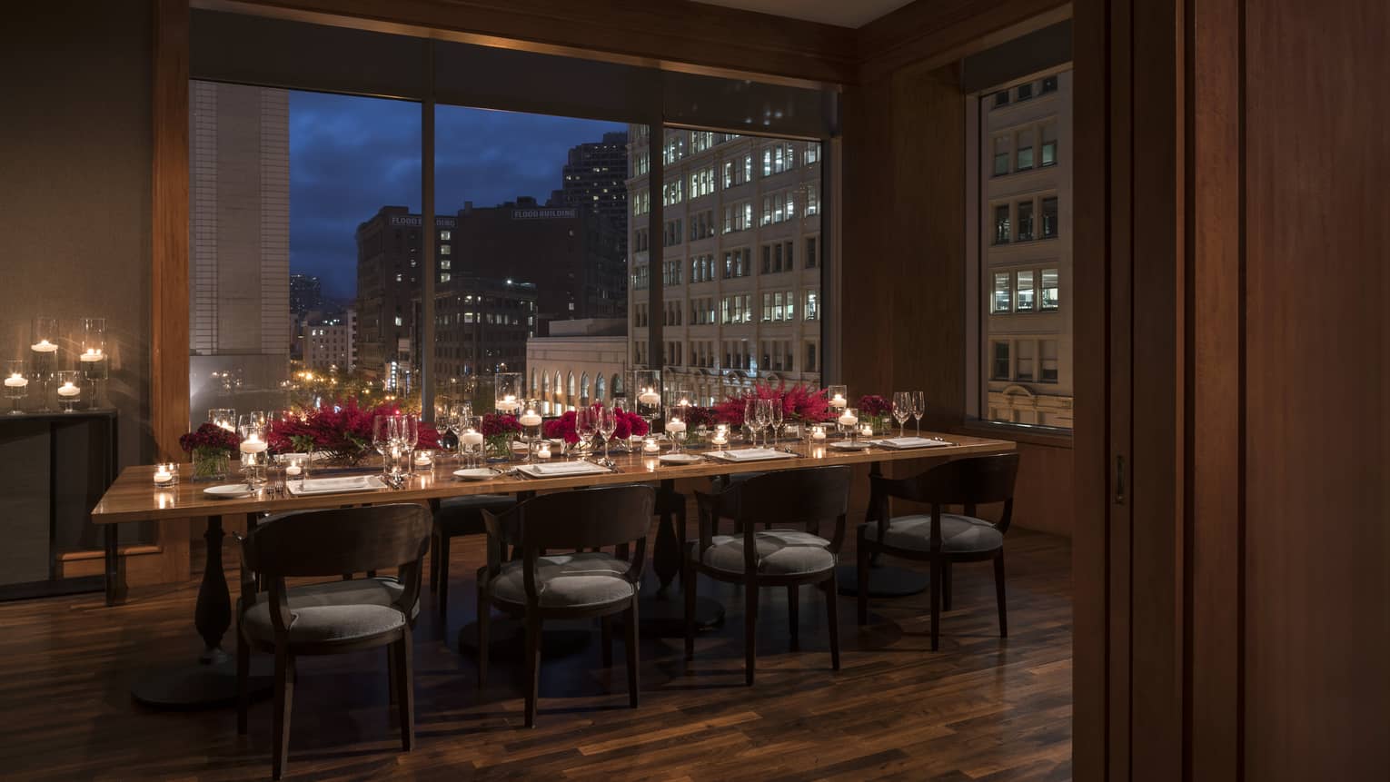 Long private dining table in dimly-lit room at night, set with wine glasses, elegant floral arrangements