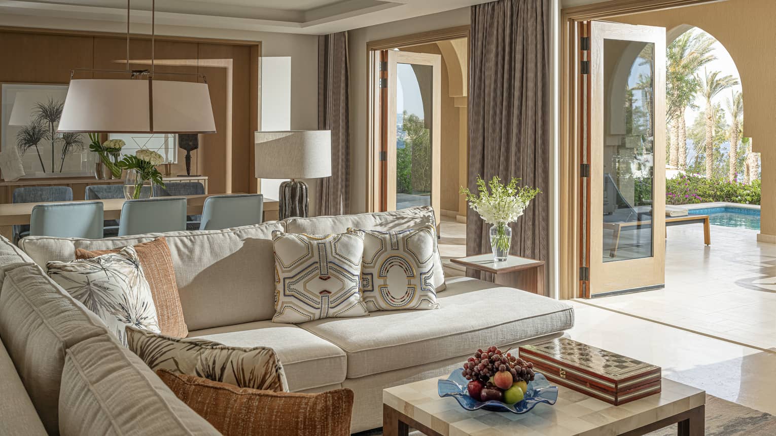 Imperial Suite living and area with cream sectional, marbled coffee table, rectangular dining table with blue chair, doorway to terrace