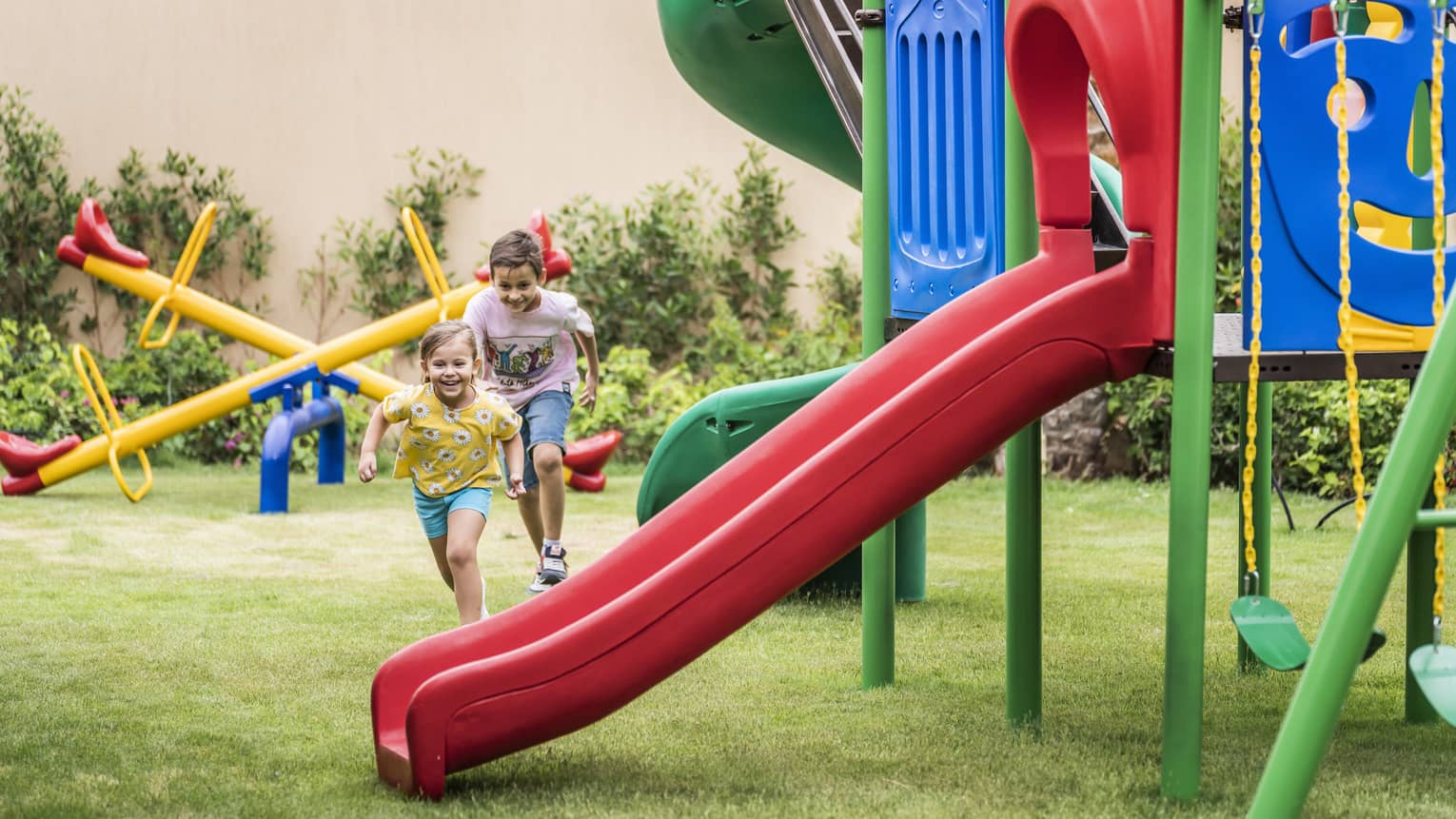 Two young boys run across a yard with playground equipment