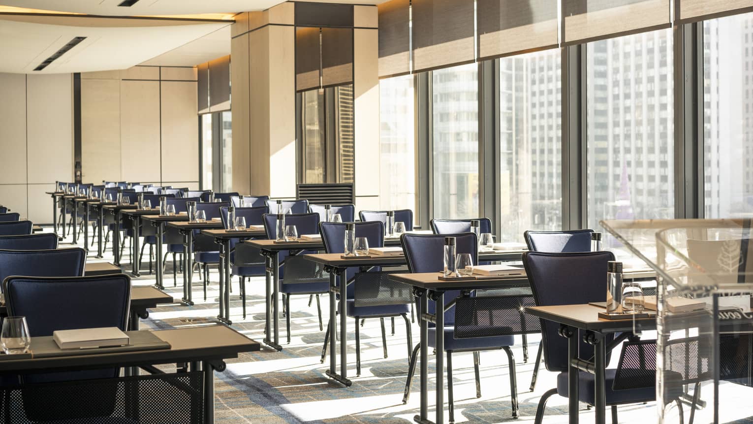 Two rows of tables with dark blue chair, glasses and notebook set up for meeting
