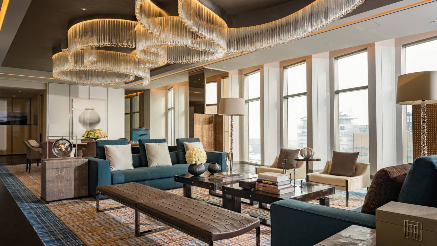 Presidential Suite seating area with large blue sofas, long leather bench, tables under modern chandeliers from soaring ceilings