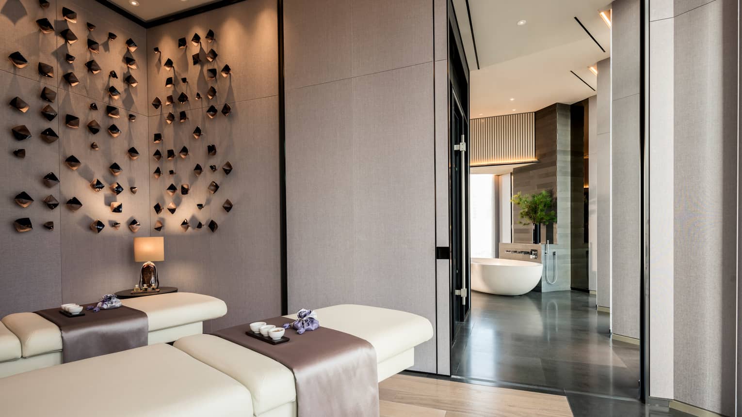 Couples massage beds under modern wall sculptures by hall leading to spa tub