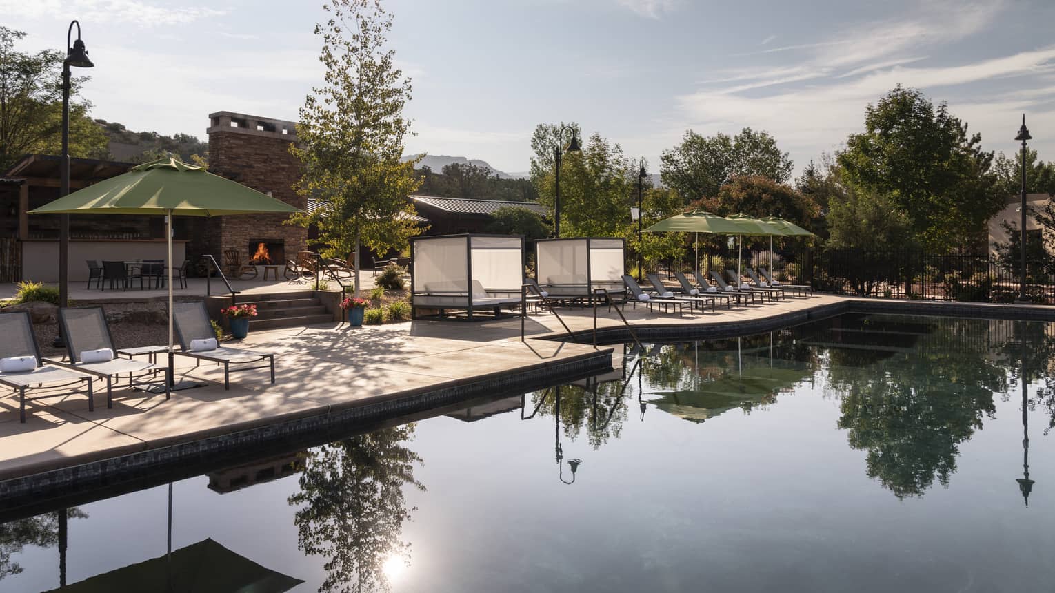 An outdoor pool with lounge chairs and green umbrellas near it.