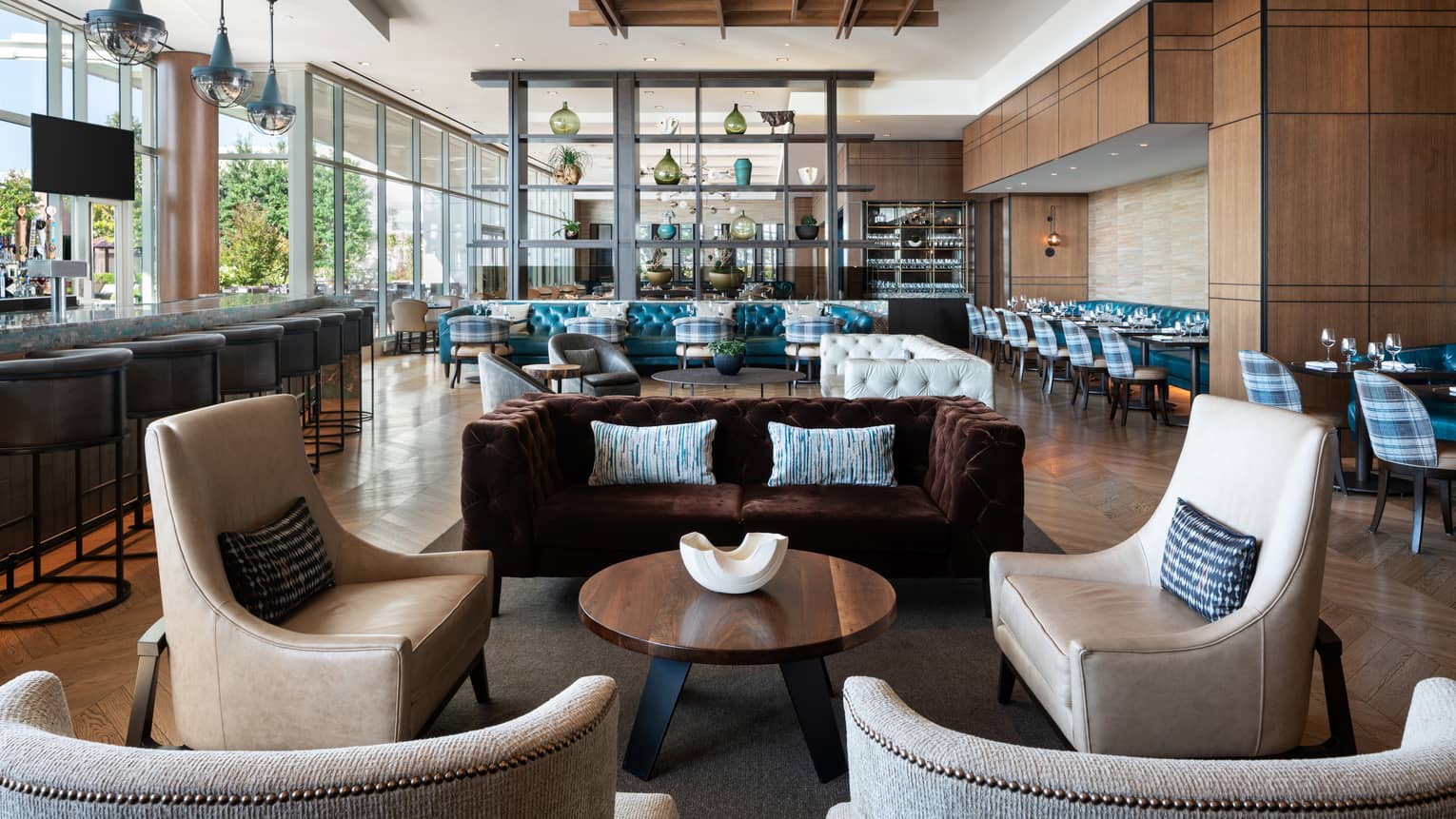 The interior of cinderhouse restaurant at four seasons saint louis is decorated with a navy accent wall, light wooden floor with a chevron style, black tables and camel colored leather chairs