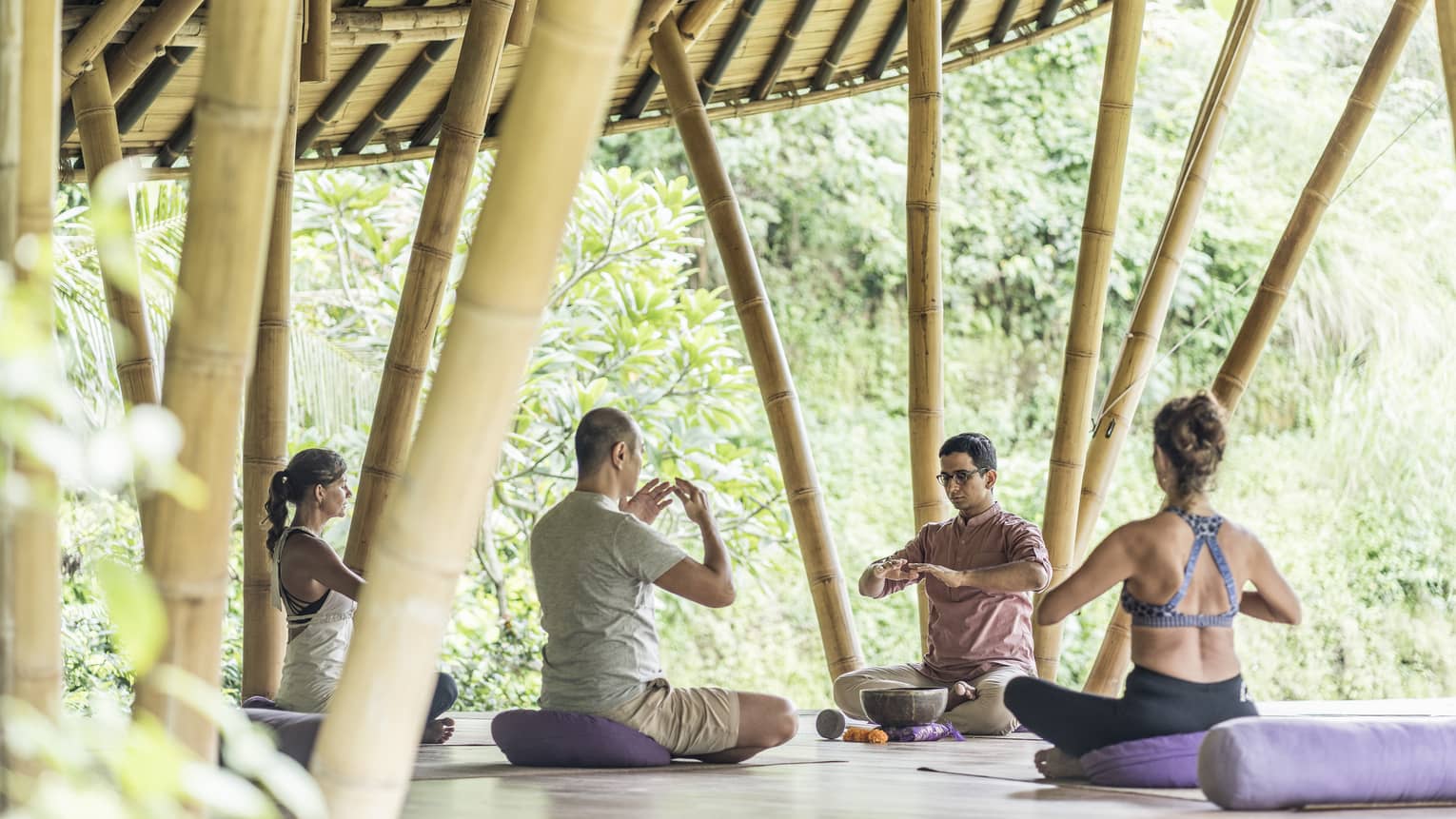 Group meditates on outdoor pavilion platform with bamboo poles