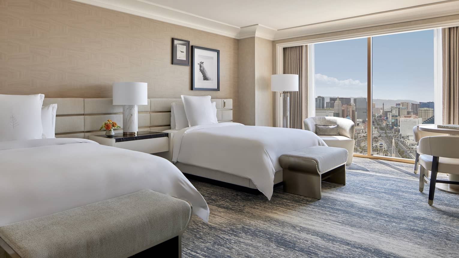 A room with two bed, a large window, and a small table with chairs.