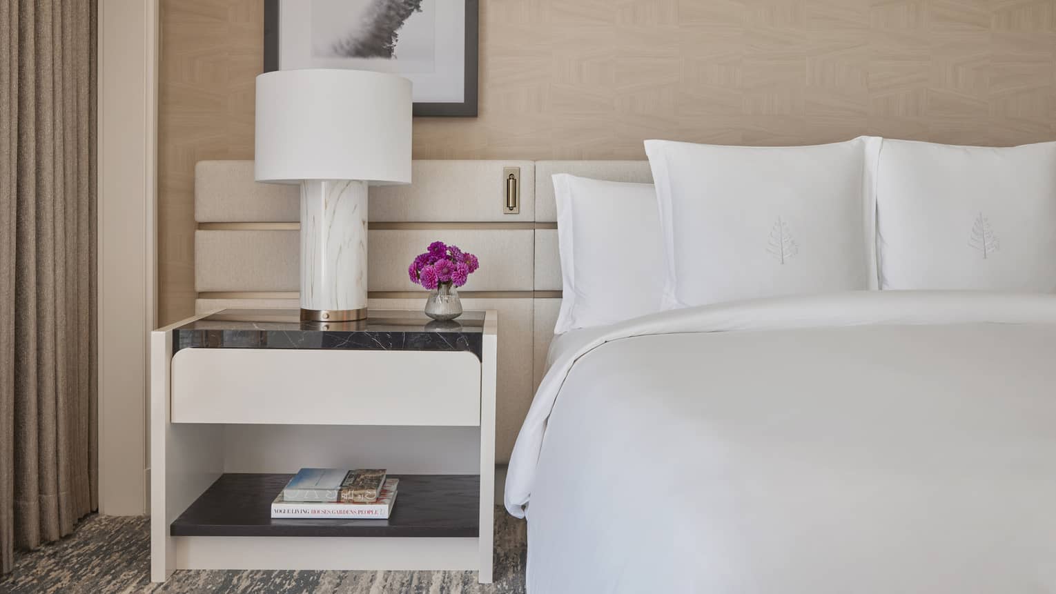 A bed in a studio room with a side table and lamp.