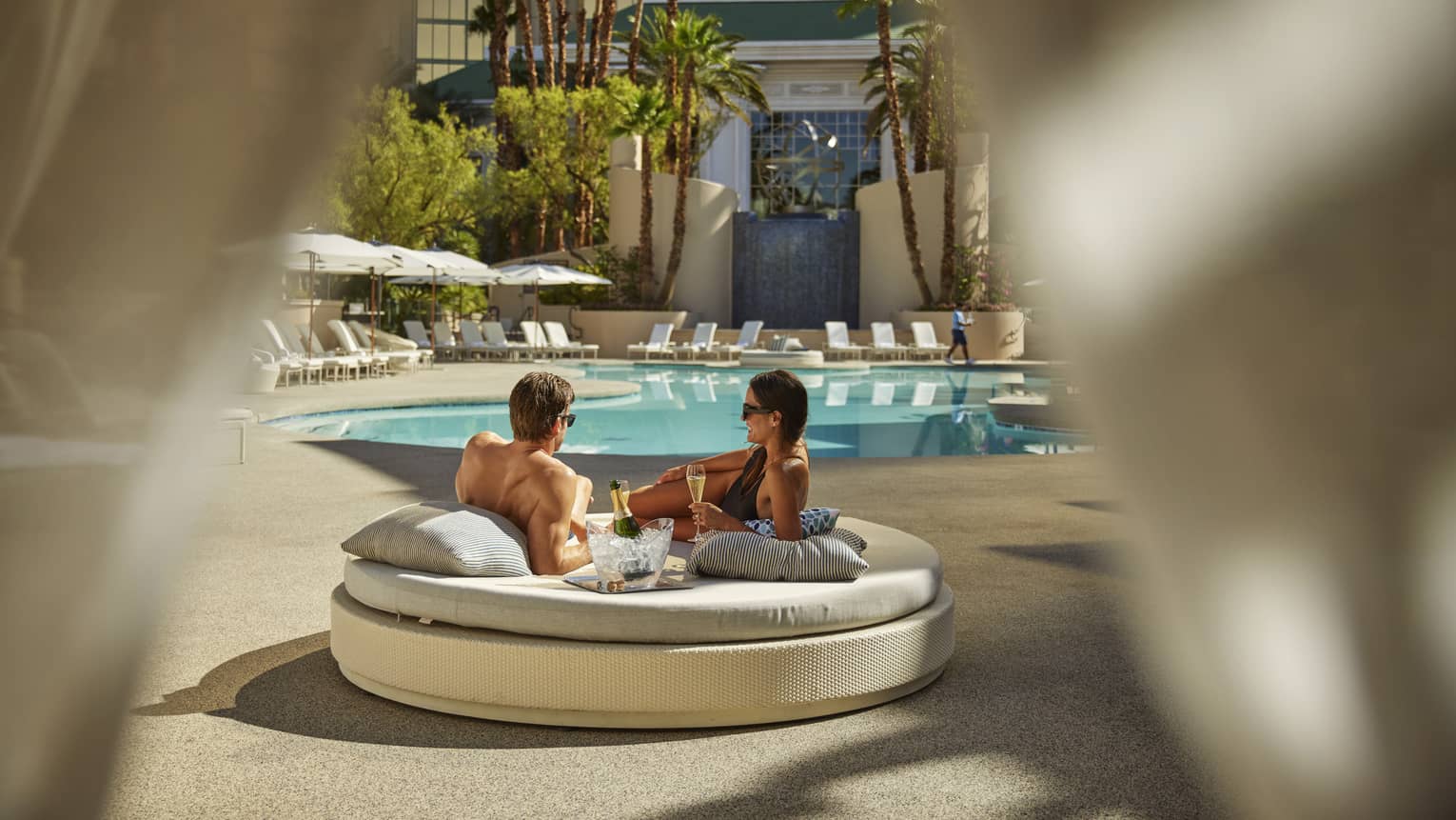 A man and woman lounging on a round daybed near a pool.