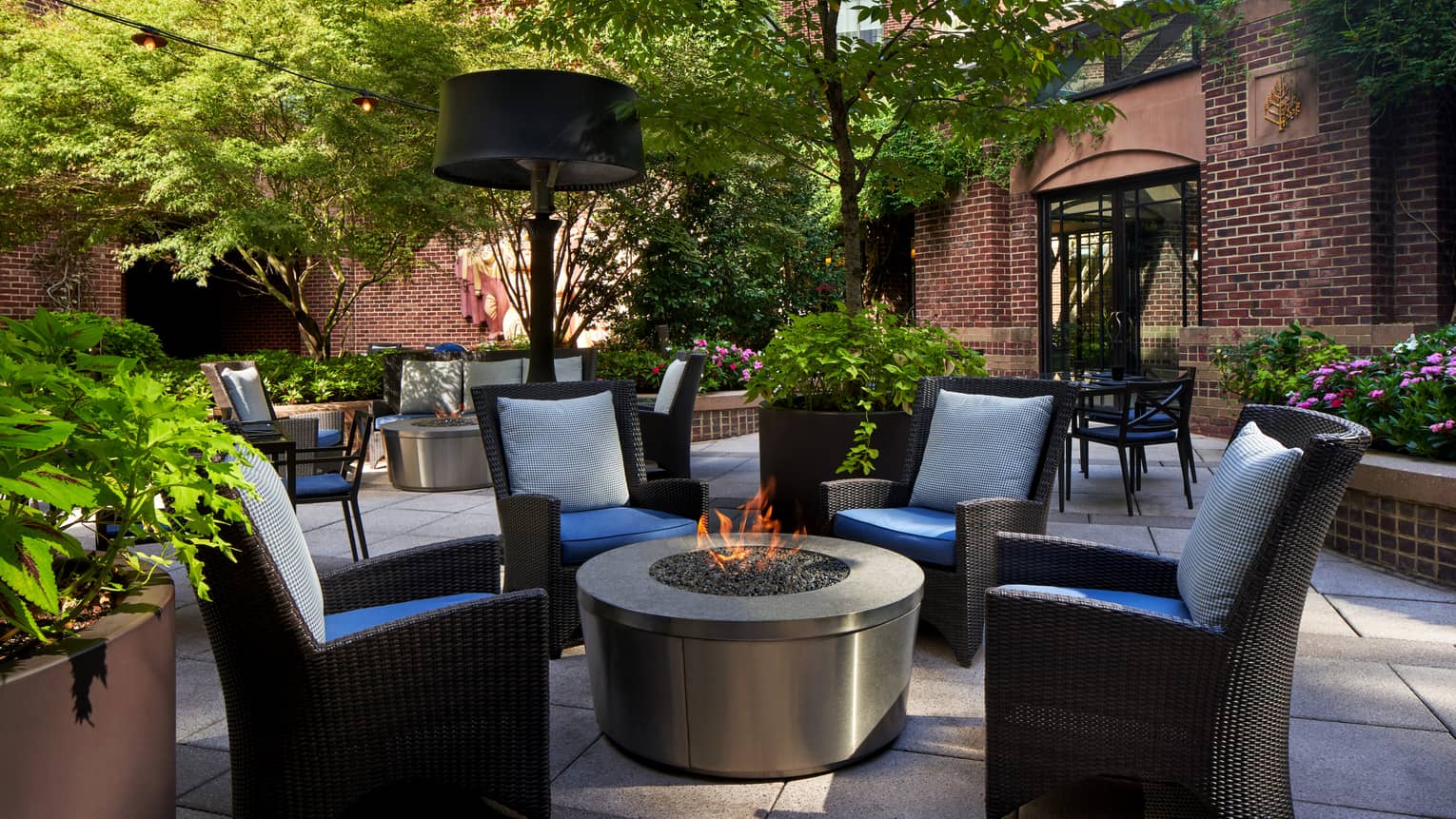 An outdoor patio area with a fire and four cushioned chairs.