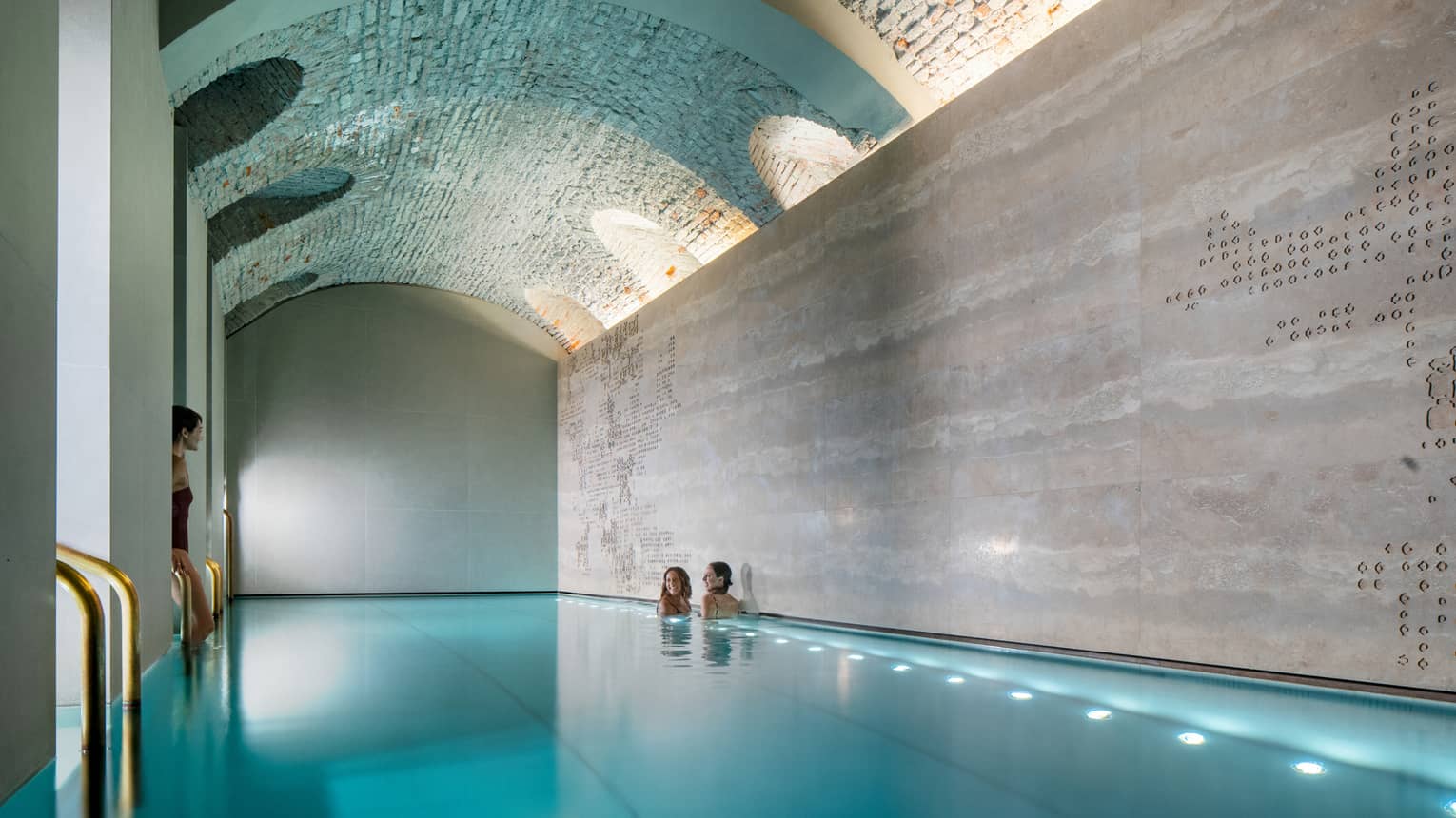 Three women soaking in a modern indoor pool with an arch ceiling
