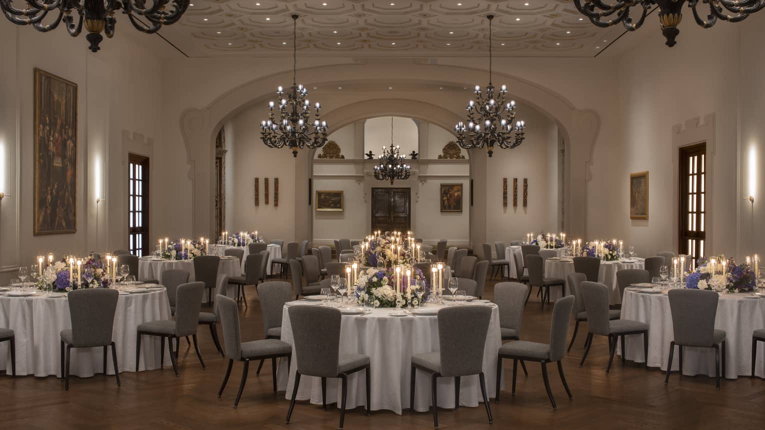Elegant ballroom with round tables and chairs arranged for a wedding, adorned with large chandeliers above