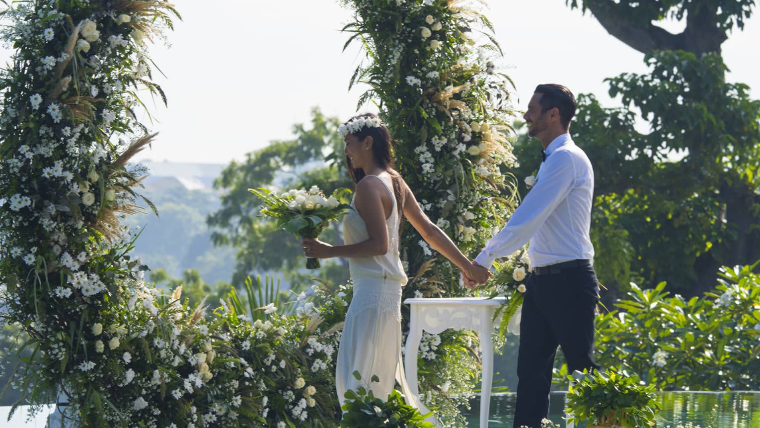 Bride holding wedding bouquet of flowers leads groom across garden