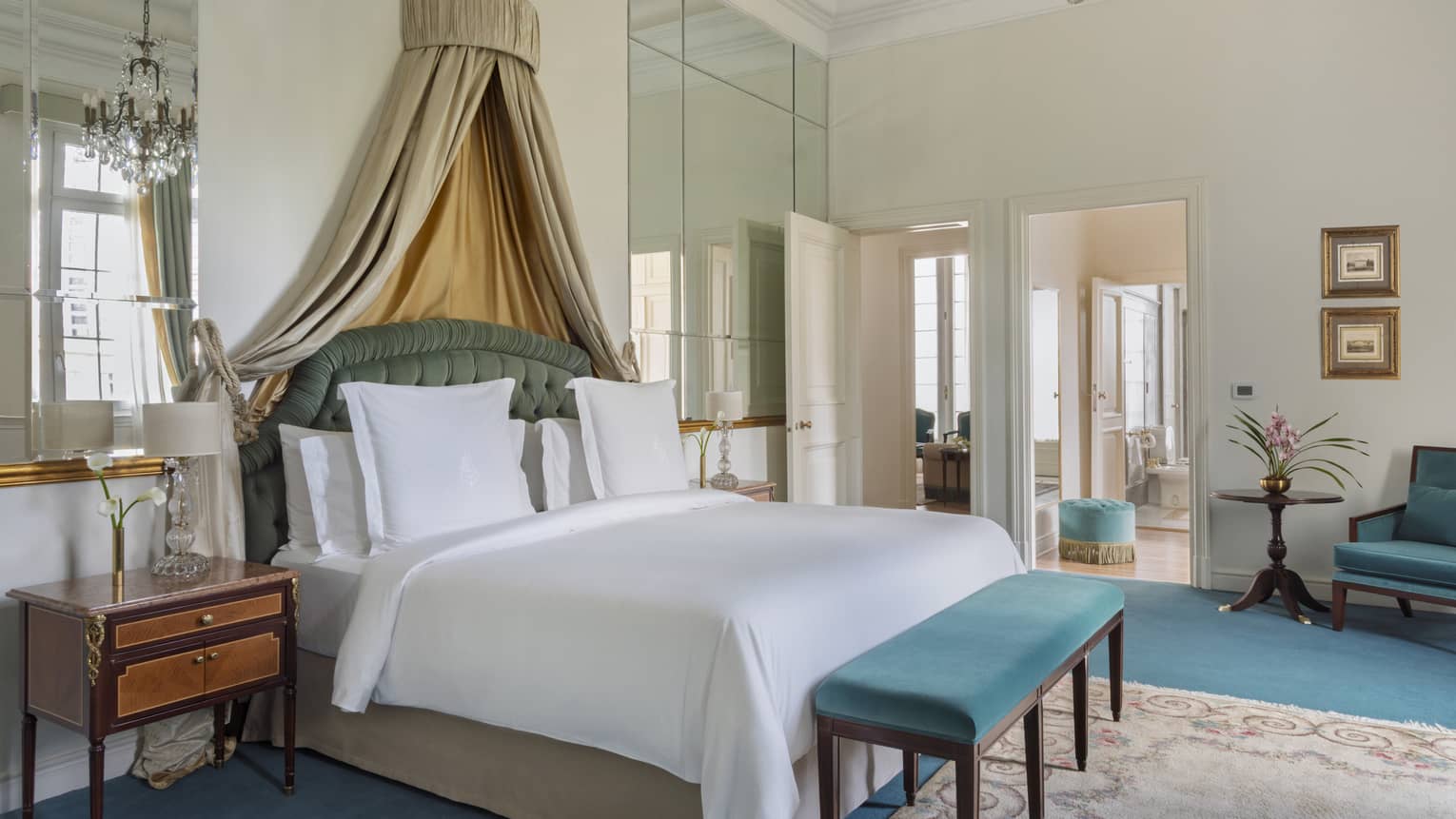 Elegant suite bedroom with king bed, draped canopy, and turquoise velvet bench and chair