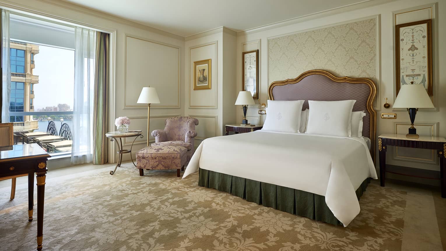Superior Room bed with padded headboard with gold trim, pink satin armchair by patio door