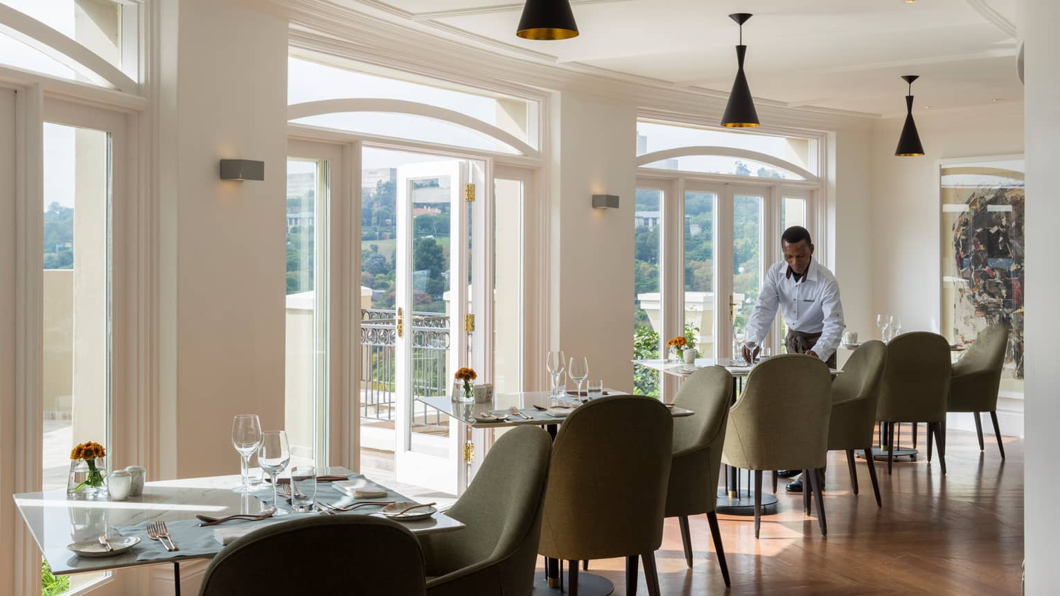 Waiter sets dining table in sunny Flames restaurant dining room