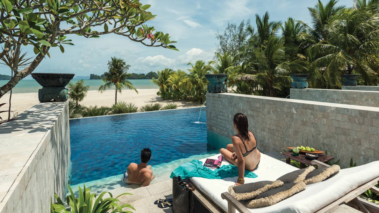 Man and woman lounge on swimming pool deck, steps, look out at beach