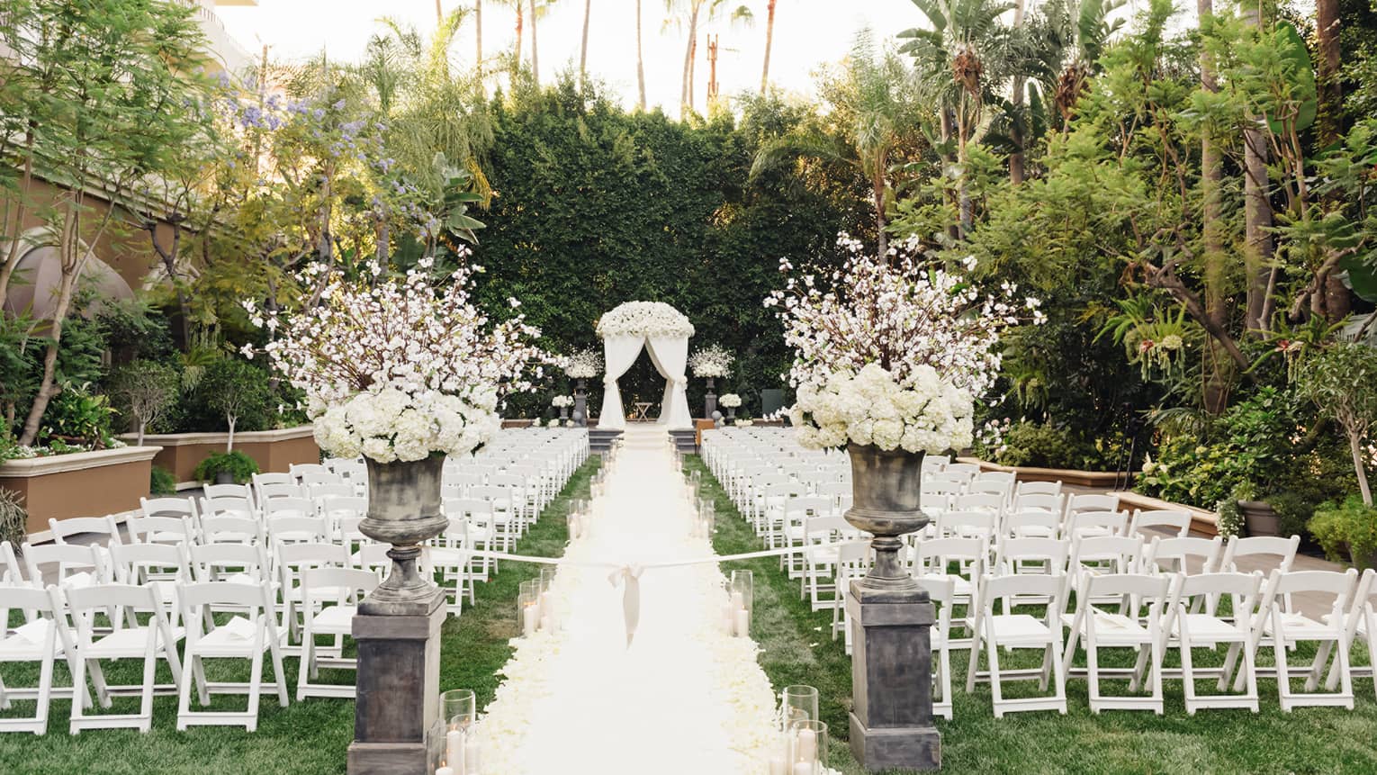 Flower pedestals by rows of white chairs leading to altar at wedding reception on garden lawn