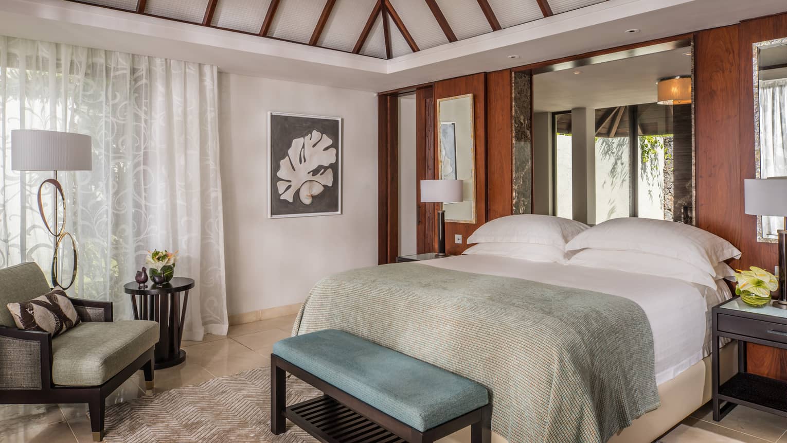 Residence Villa bed with light blue blanket, bench, armchair by drawn sheer white curtains