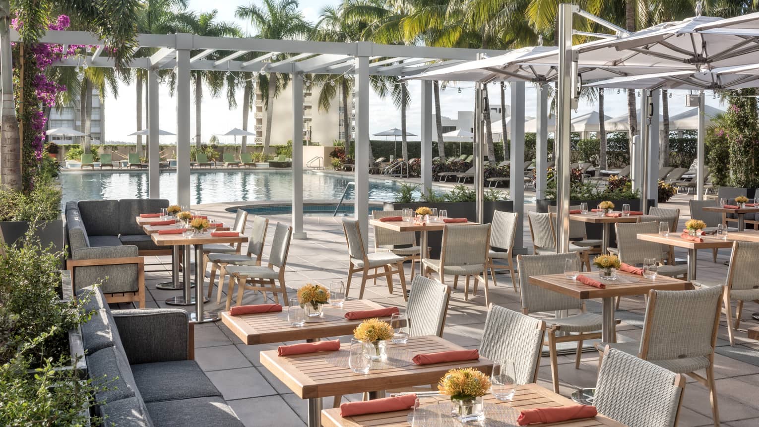 Patio dining tables under white pergolas by swimming pool