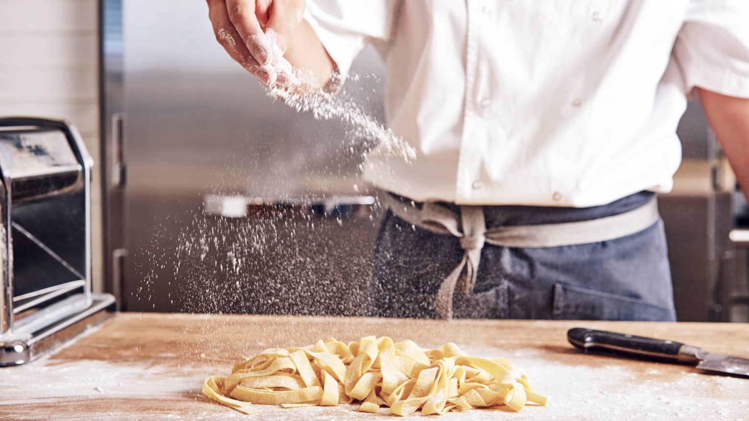 Noe chef sprinkles white flour over thick fresh pasta noodles on counter