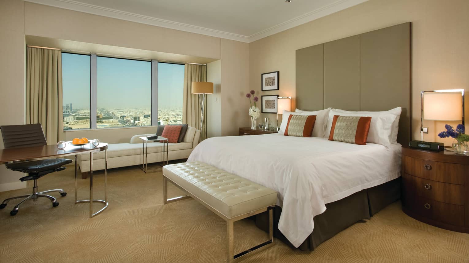 Superior Room side view of bed with tall padded headboard and leather bench, beige carpet, long chaise at window