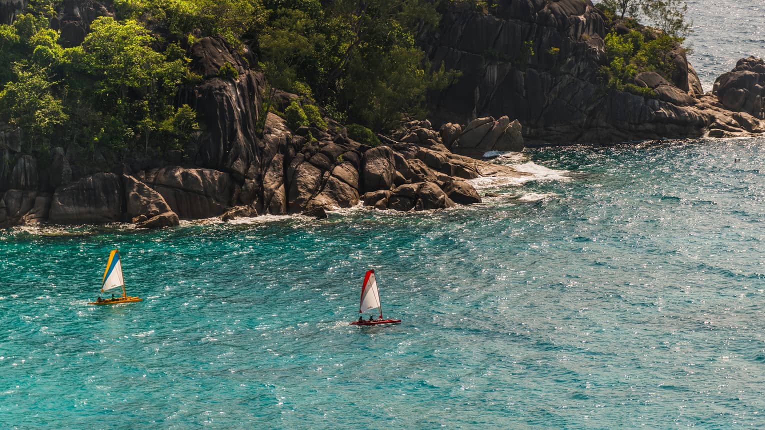Aerial view of two sailboats in turquoise lagoon in front of rock cliffs, green trees