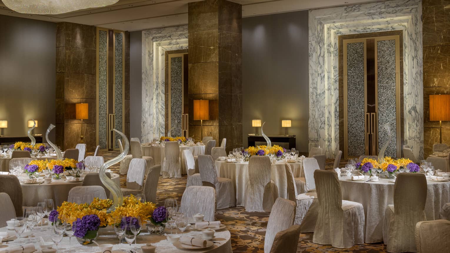 Ballroom with marble doorways, round banquet tables with purple and orange flowers, linen-covered chairs