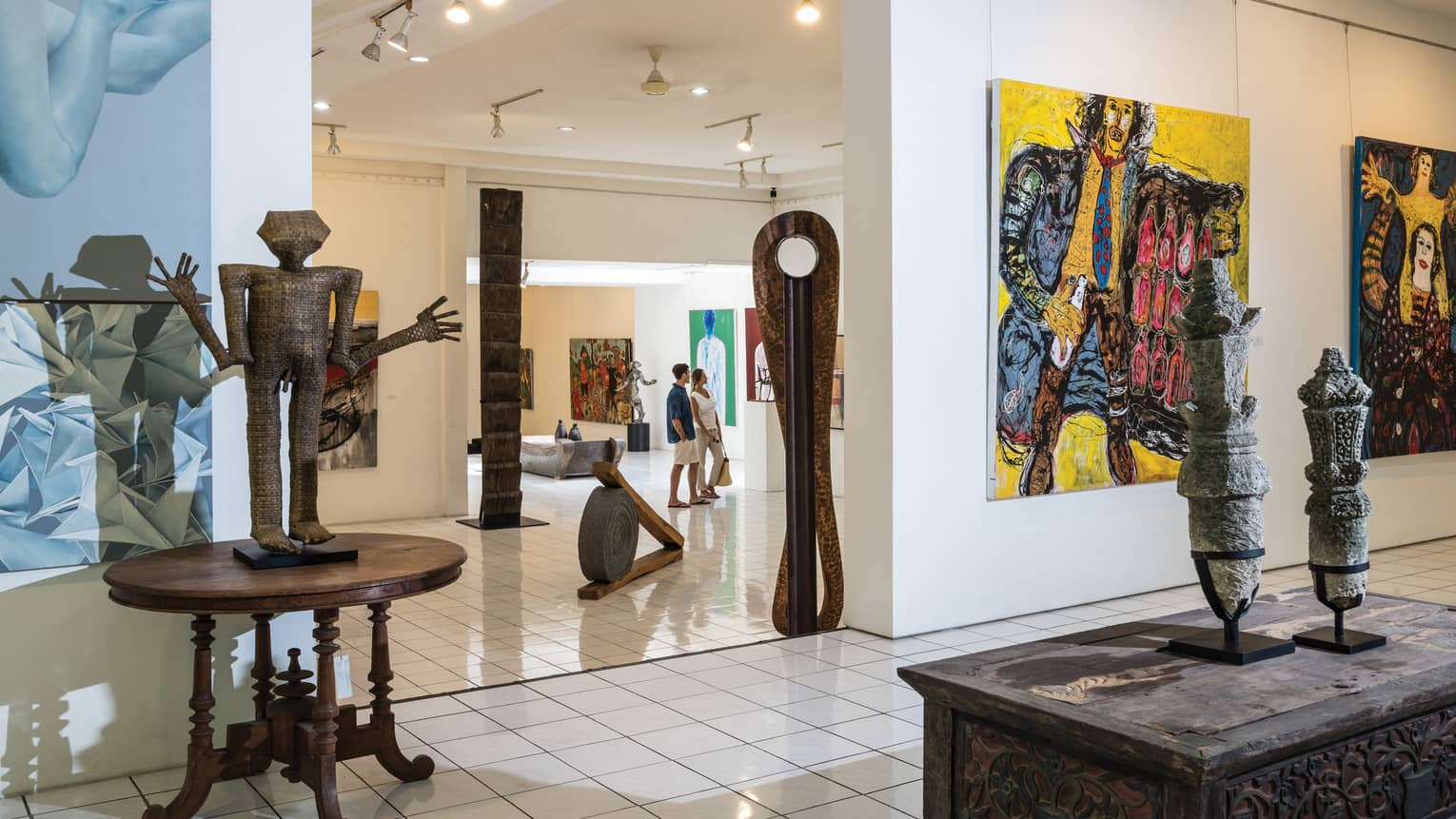 Couple walks through bright, modern art gallery with large sculptures, colourful paintings