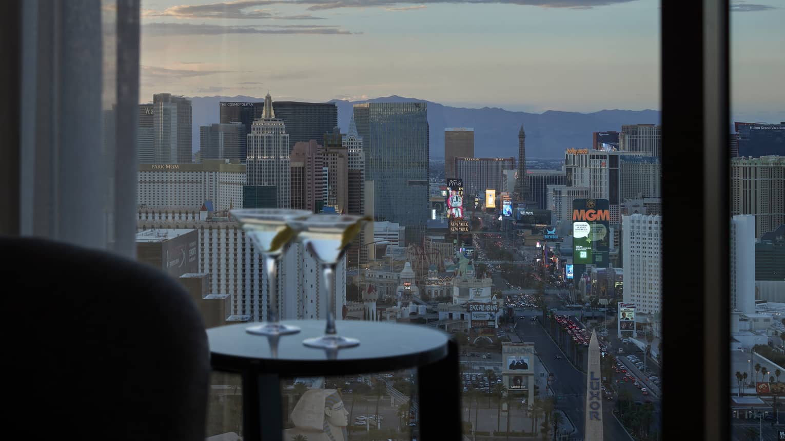 Two cocktail on a small table near window looking out at the city.