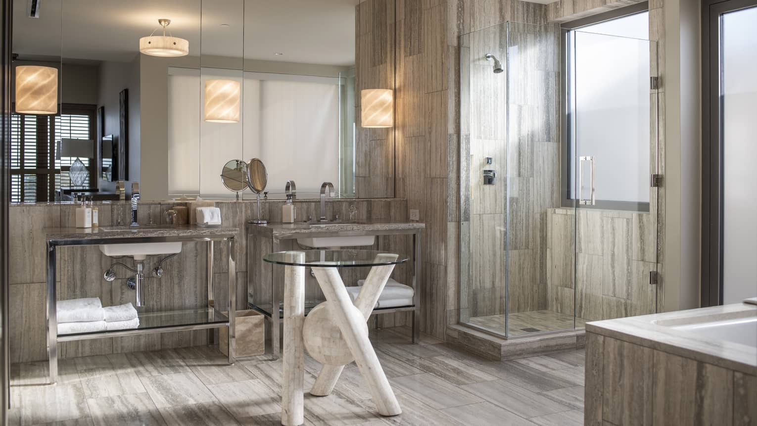 Modern bathroom with glass shower, dual sinks, large mirror and neutral stone finishes.