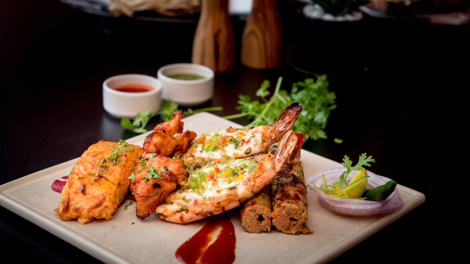 Seafood and meat kebabs garnished with fresh herbs on white platter