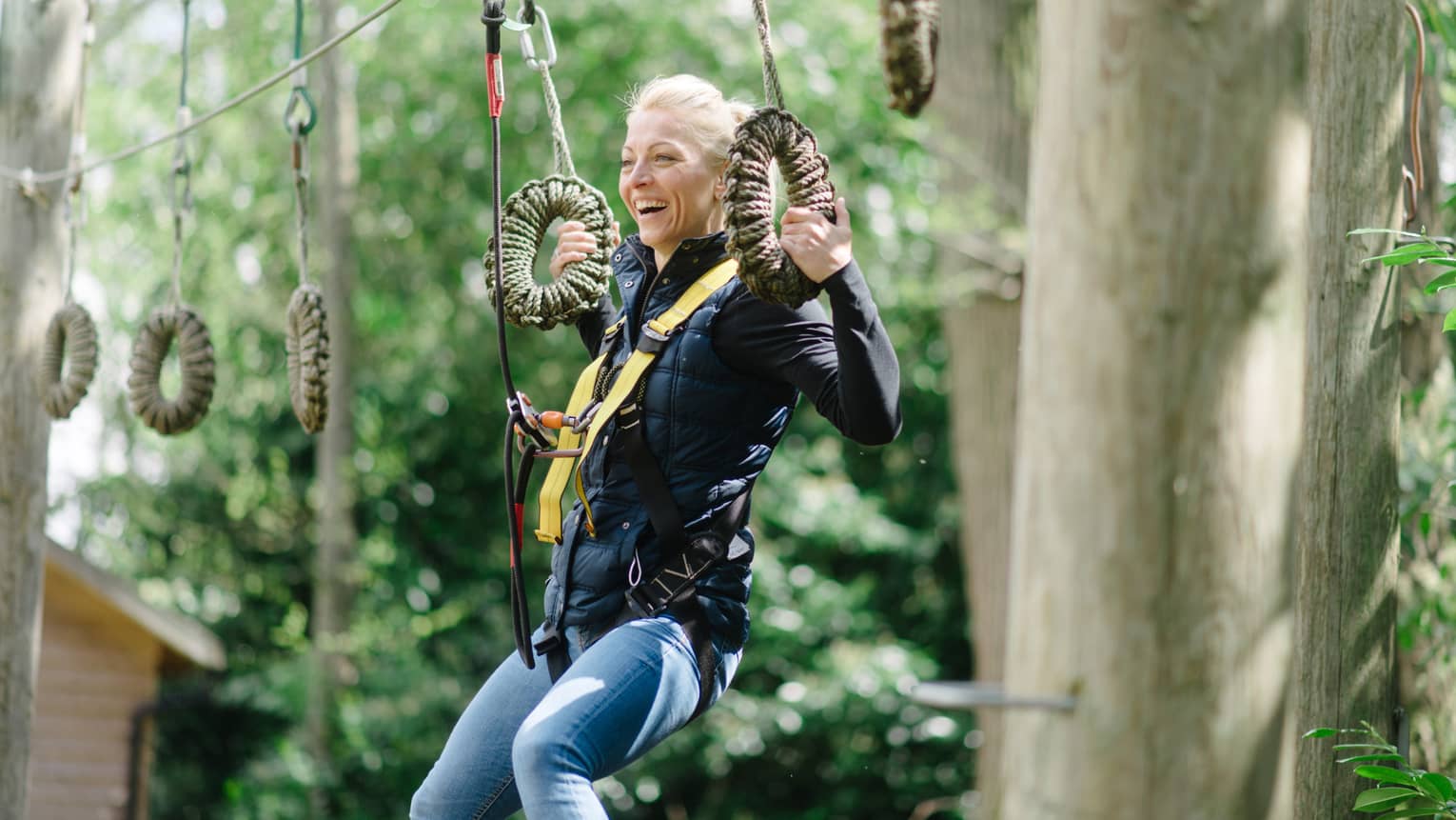 Women in yellow harness hanging onto highwire rope between trees