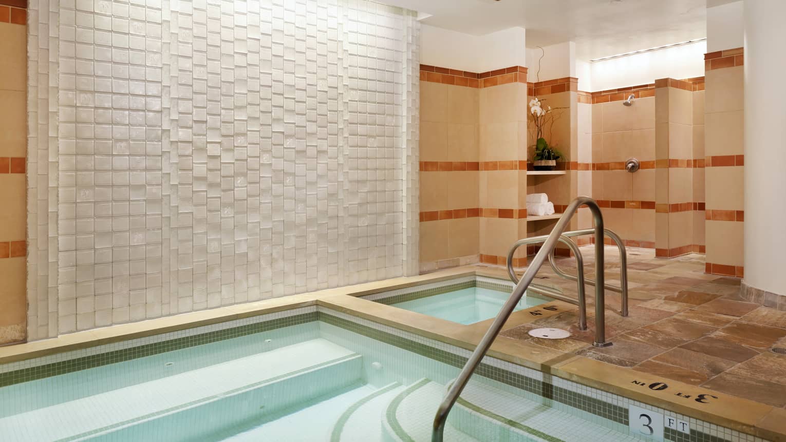 Corner of a rectangular indoor pool with a handrail and tiled floor
