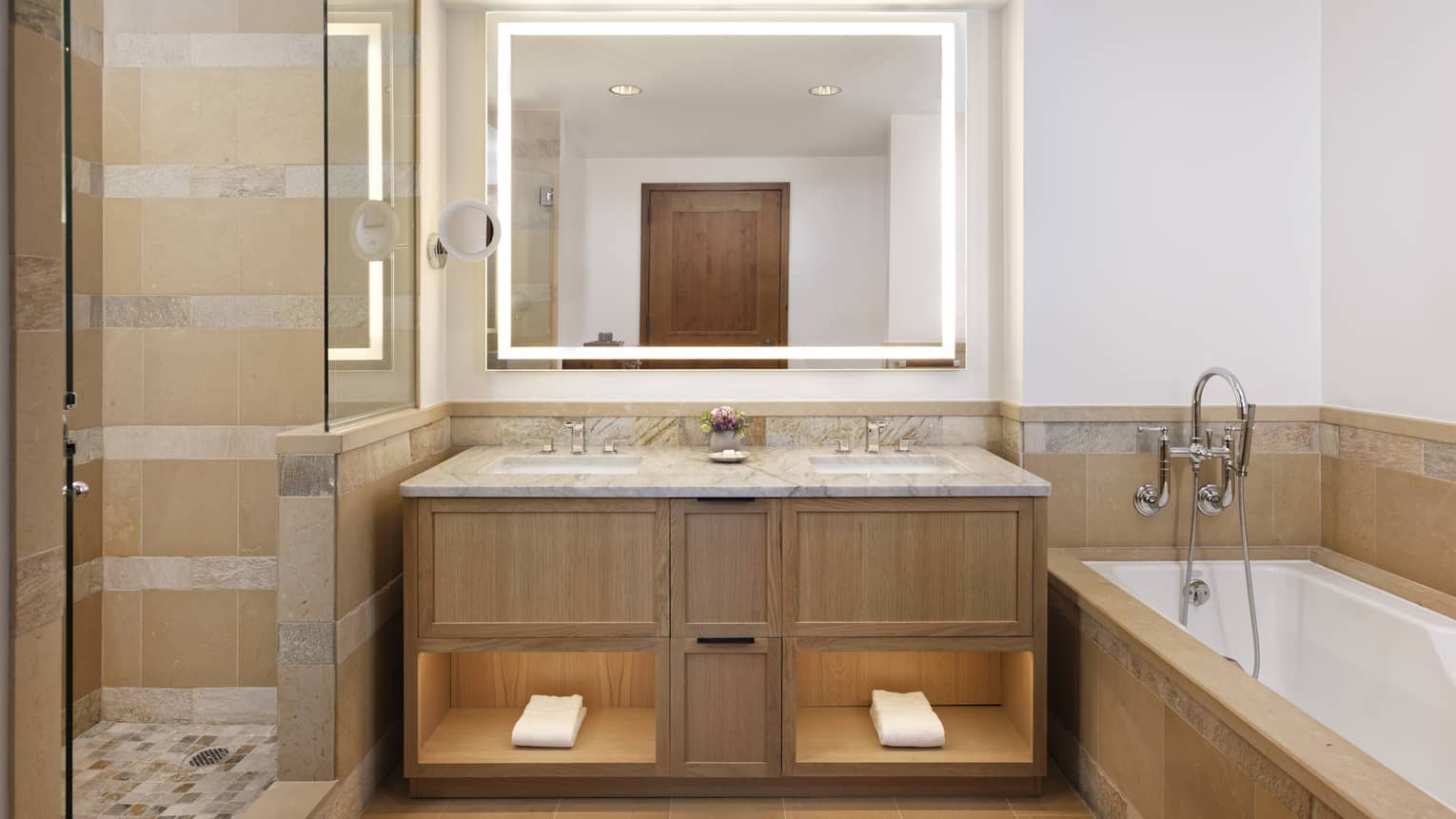 Bathroom with a dual-sink wooden vanity with marble countertop, backlit mirror, walk-in shower and soaking tub 