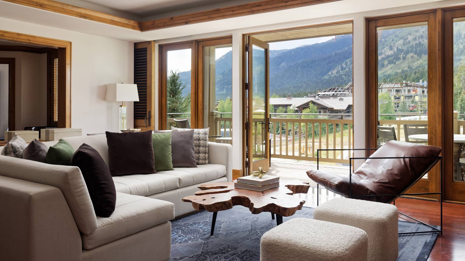 A room with a large sofa, coffee table, chair and large window looking out at mountains.