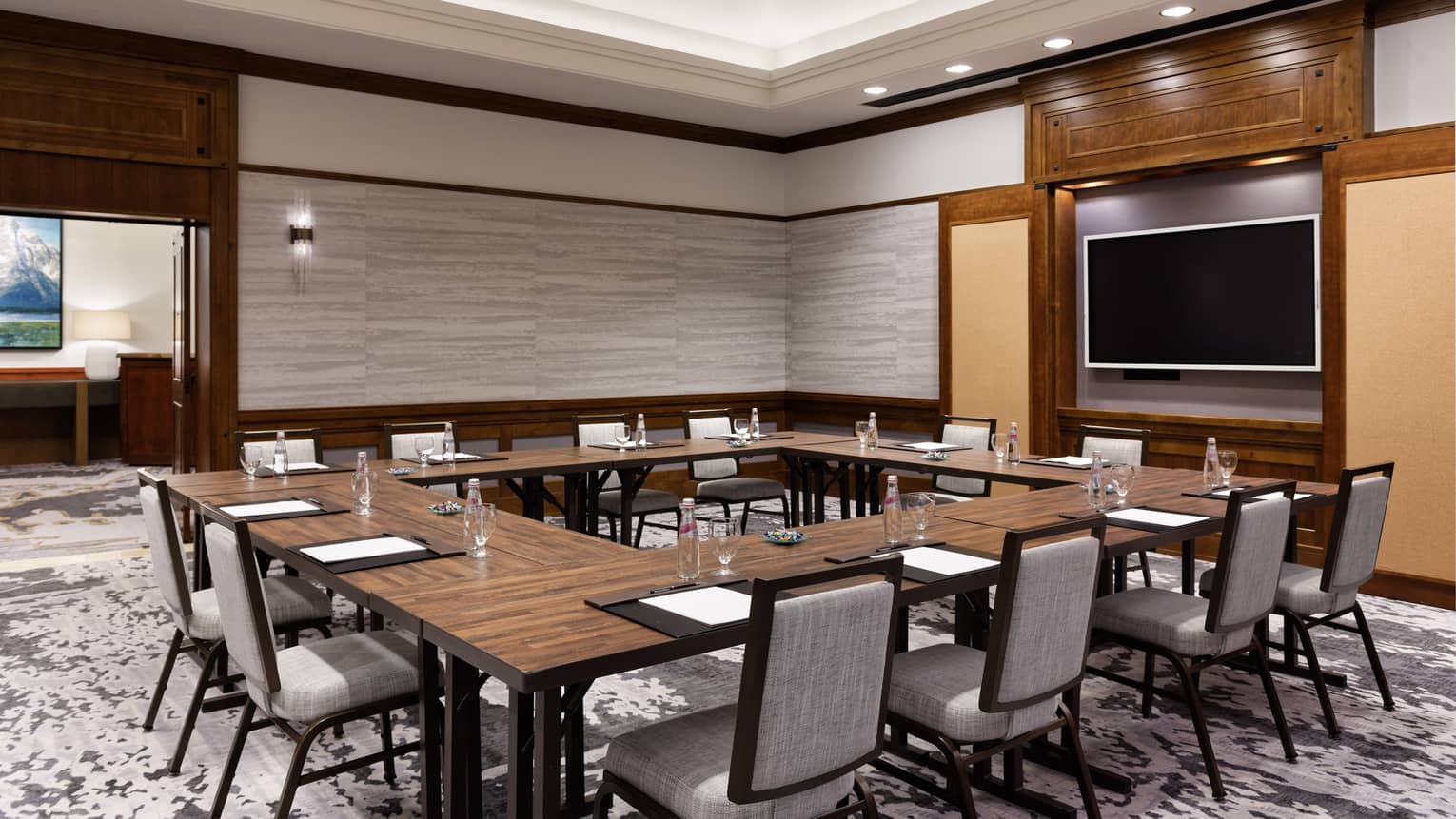 A meeting room with a large square table, chairs and a screen on a wall.