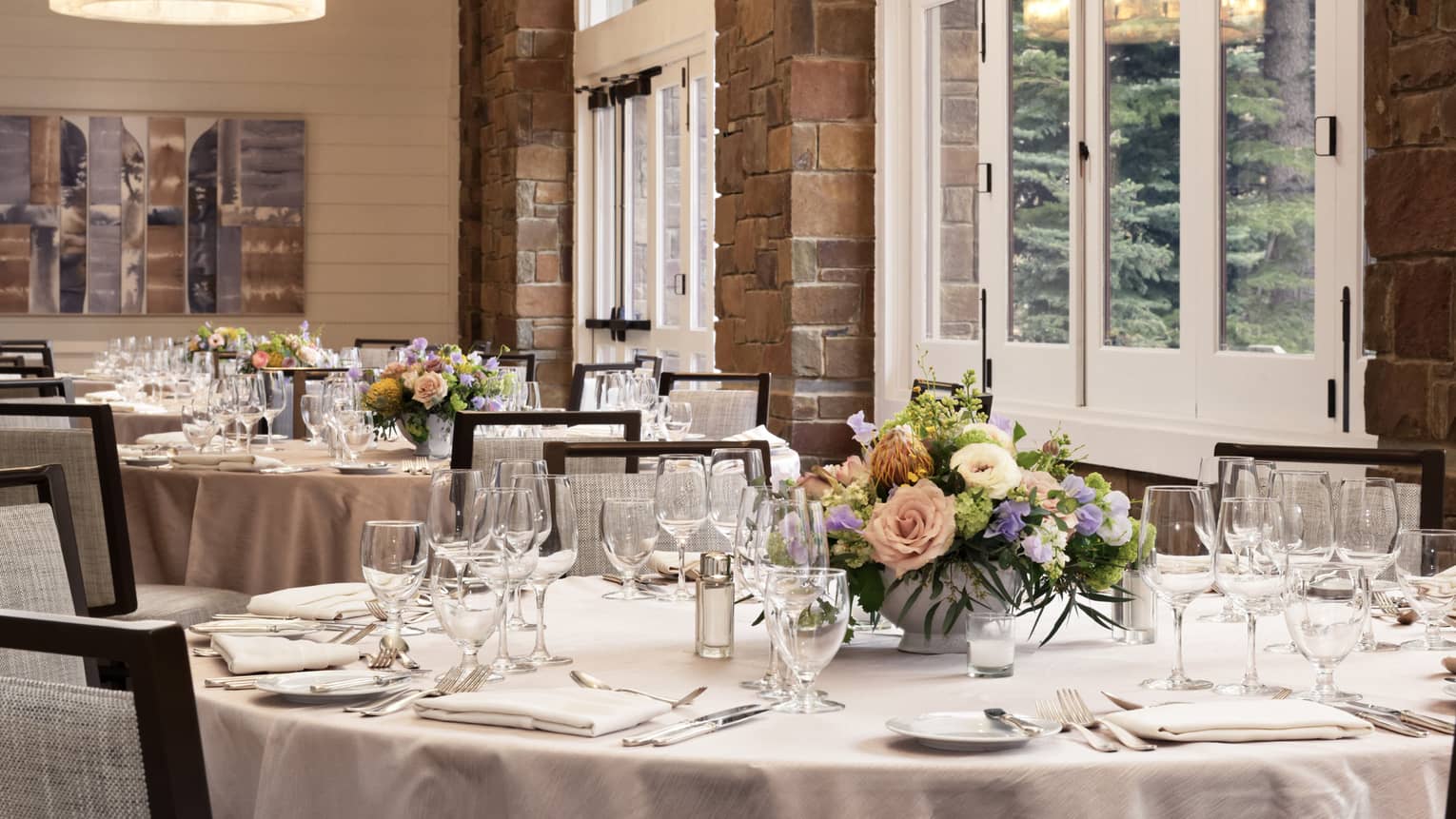 An event room with tables set with glasses, silverware and flower bouquets