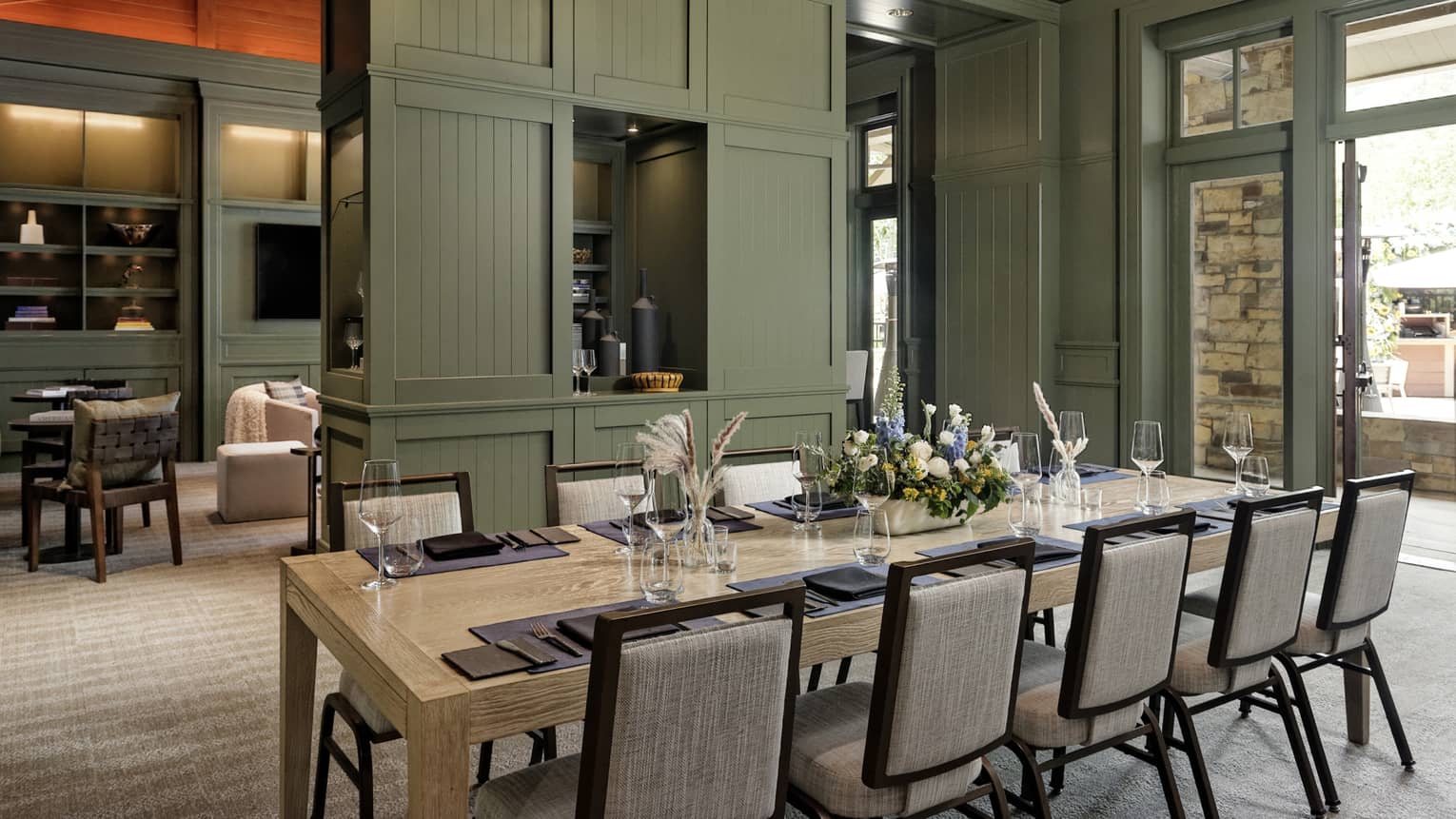A dining room with green walls and a table set with flowers, glasses and place mats