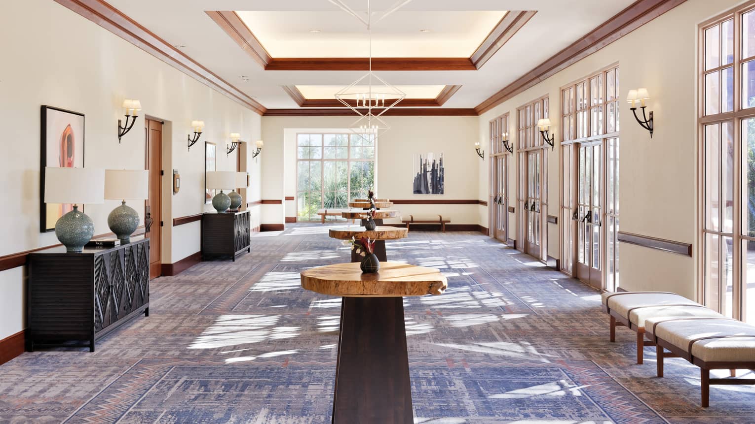 A lobby area with standing tables, shelves with lamps, and benches along large windows.