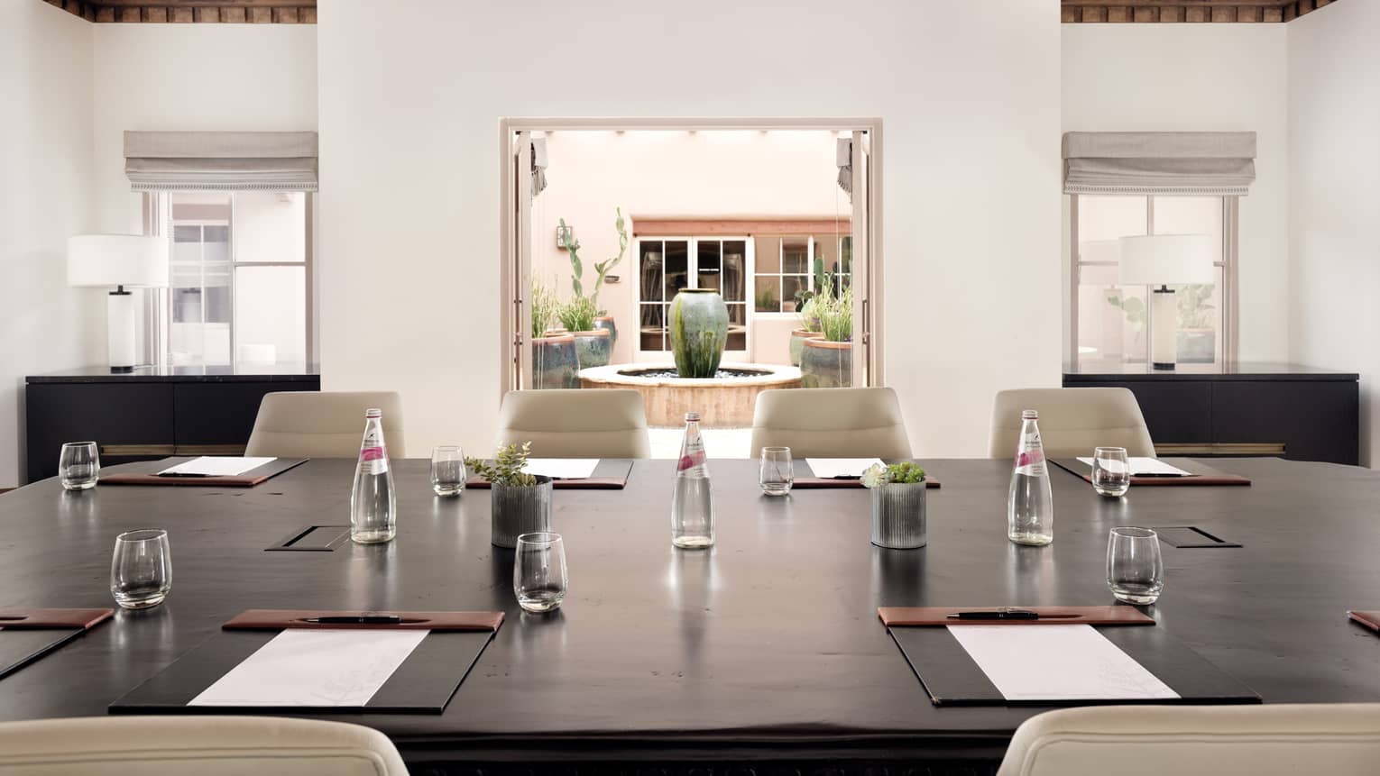 A boardroom with a large wood table with a view of a courtyard outside.