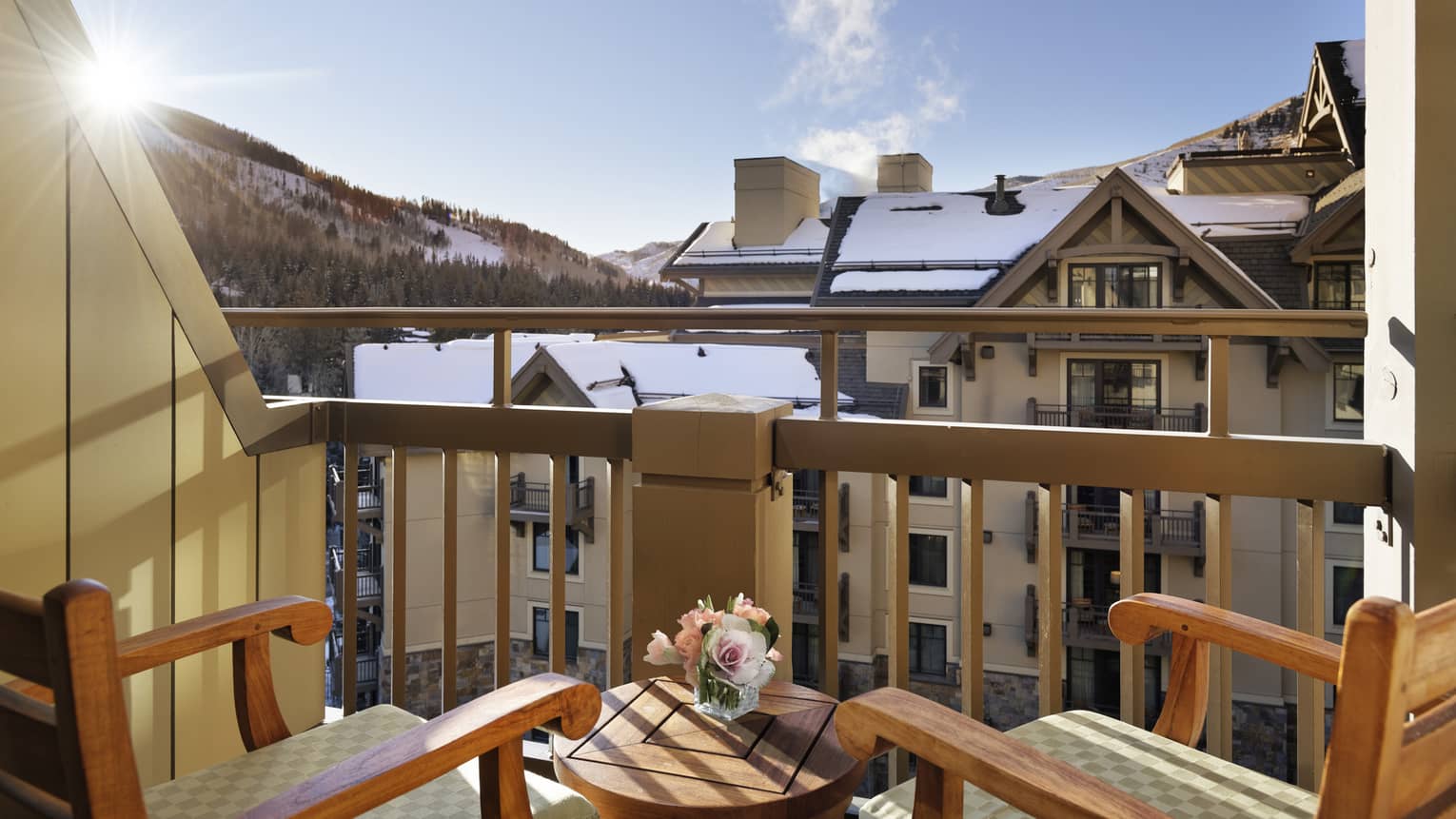 A balcony with two wooden chairs looking at cabin like buildings and a mountain in the distance.