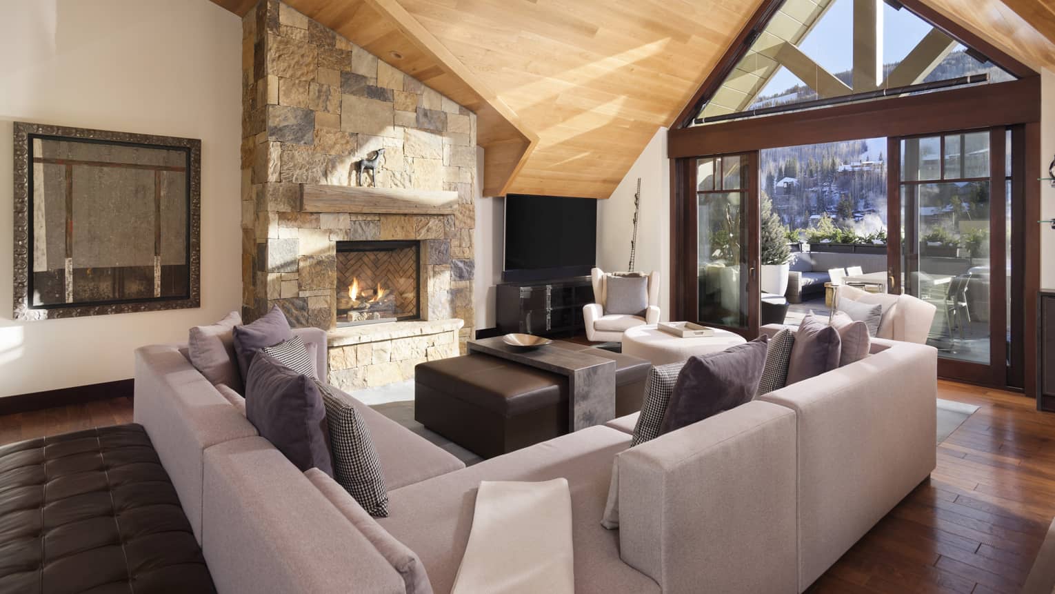Living room with grey sectional, wooden vaulted ceiling, large window, stone hearth