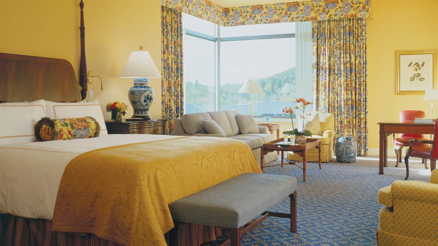 Corner Studio Suite bed with embroidered gold blanket, blue bench, sofas by corner window