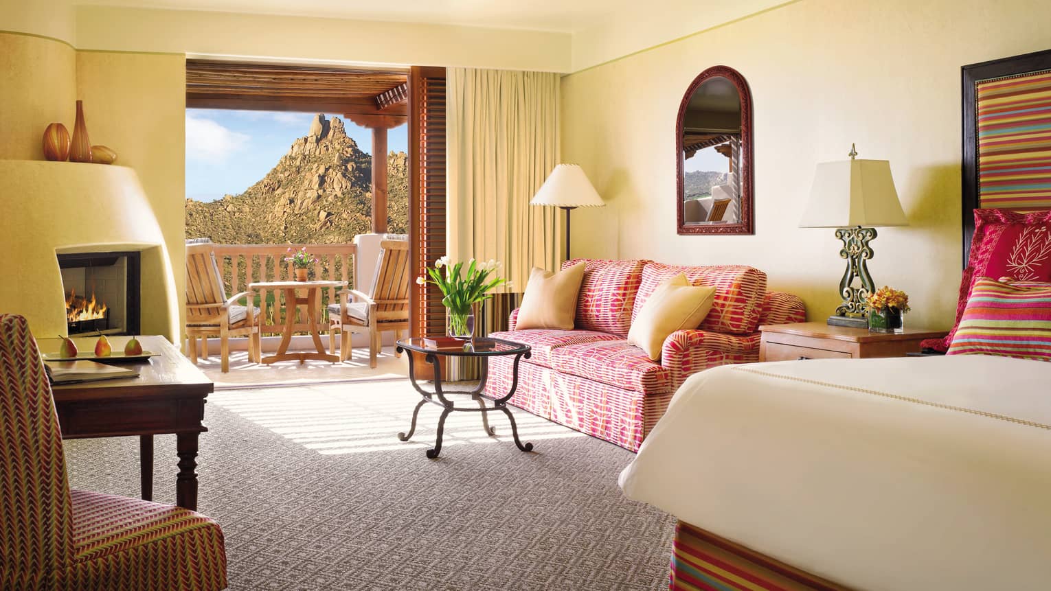 Deluxe Casita Room corner of bed, pink patterned loveseat and table by open balcony door, mountain view