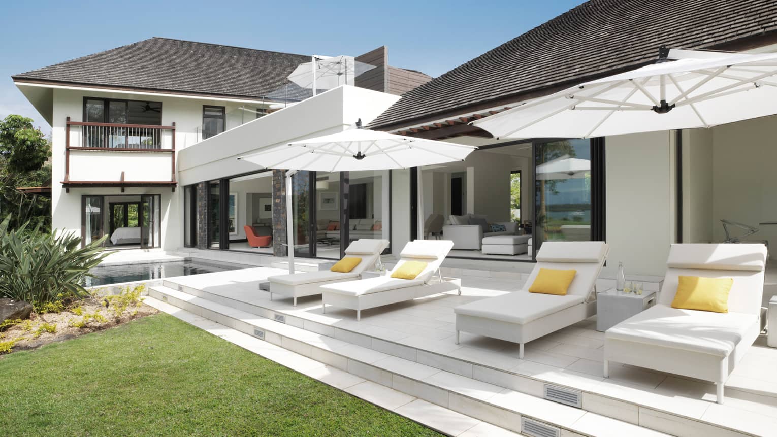 White lounge chairs under umbrellas on patio in front of large white two-storey villa