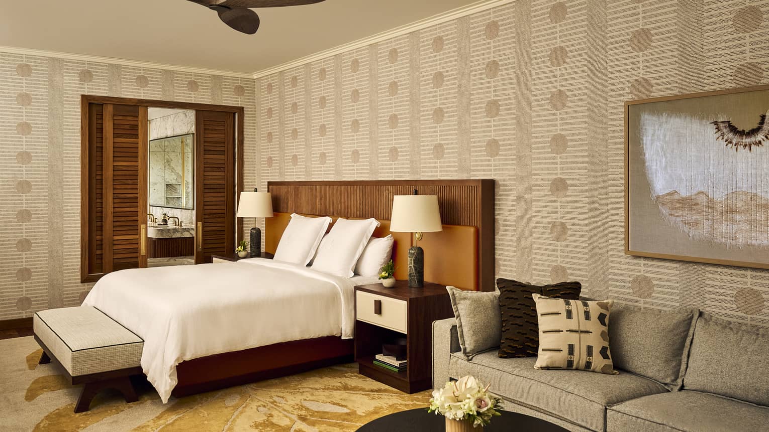Resort bedroom with single bed and sofa, plus a ceiling fan and shuttered doors leading into bathroom