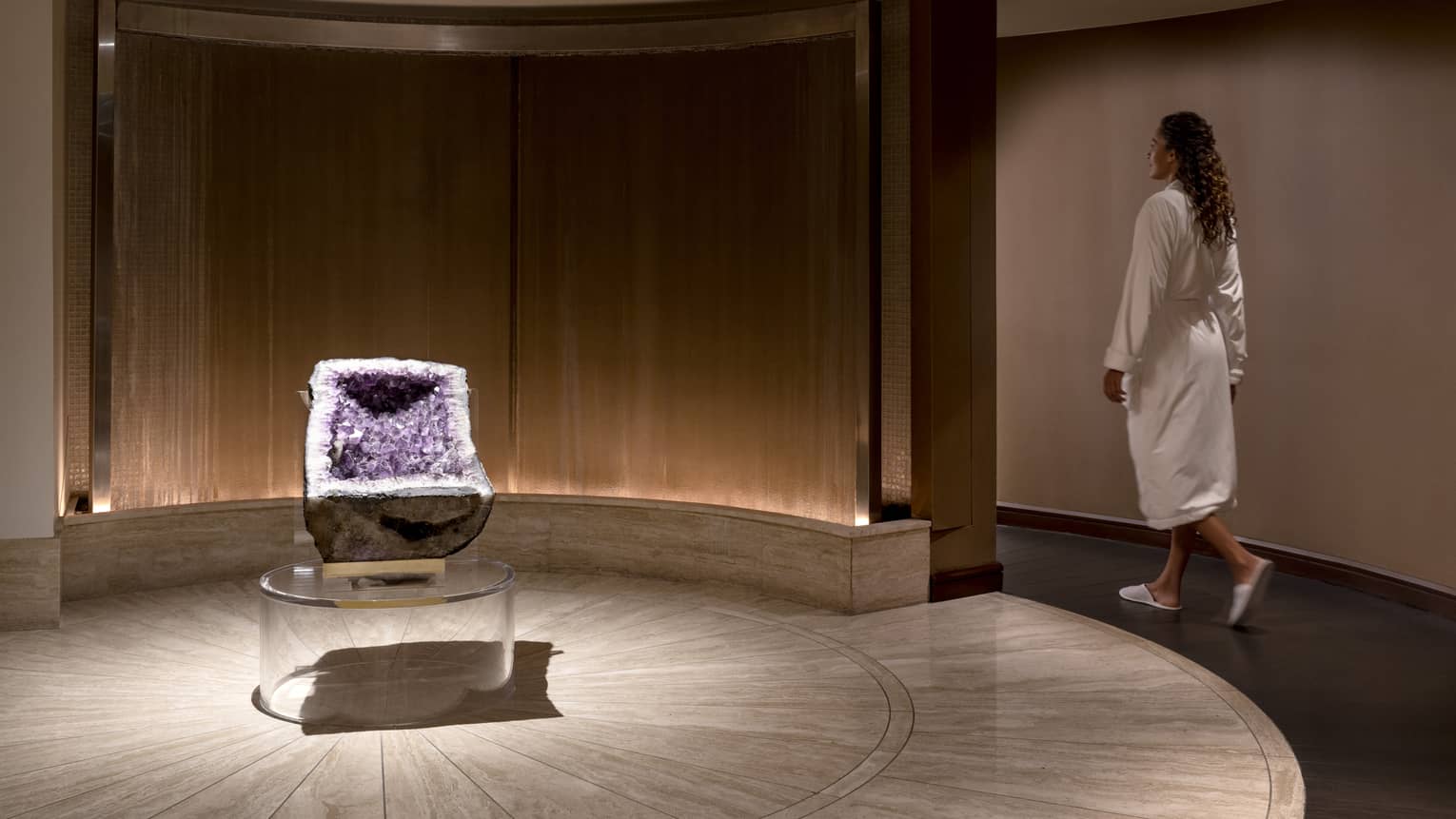 Woman wearing robe walking in room with a purple crystal displayed.