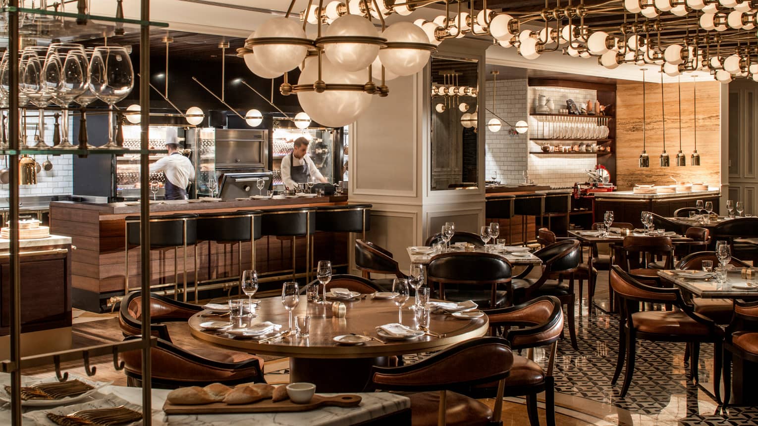 La Capitale dining room with dark, wood decor, round tables and chandeliers, globe chandeliers, chefs in open kitchen